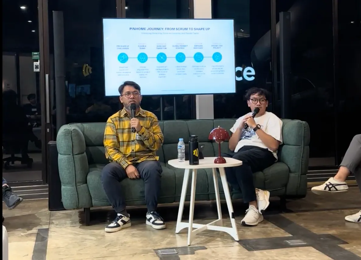 Hazmi and Richard Dharmadi holding microphones beside a slide on Pinhome’s journey from Scrum to Shape Up.